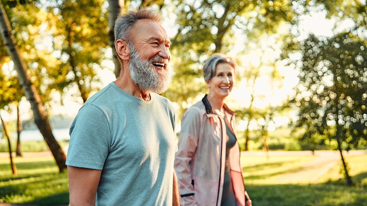 Hobby active in retirement. Caucasian man of gray hair with beautiful woman walking to Summer Park and smiling joyfully. The retired couple of fitness in sports dresses rested after dawn: used in a piece about vitamin D capable of protecting telomeres and supporting longer life