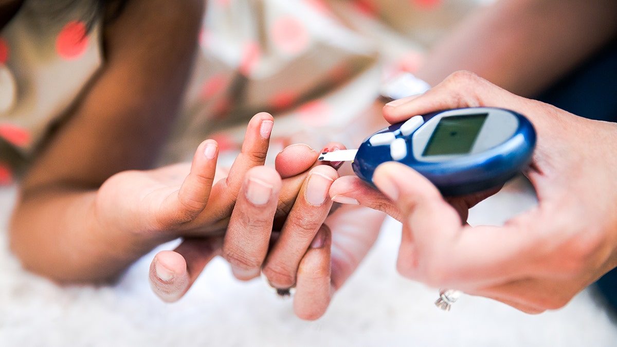 Mother checks the child's diabetes by monitoring blood glucose