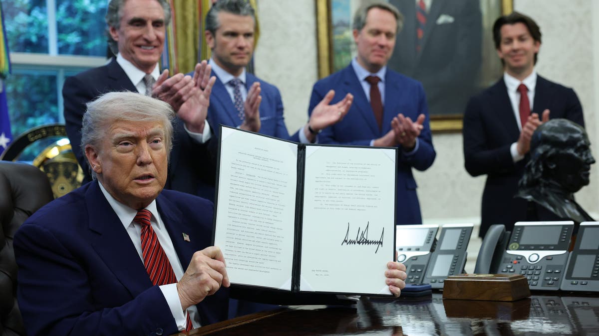 President Trump, sitting, shows the signed document
